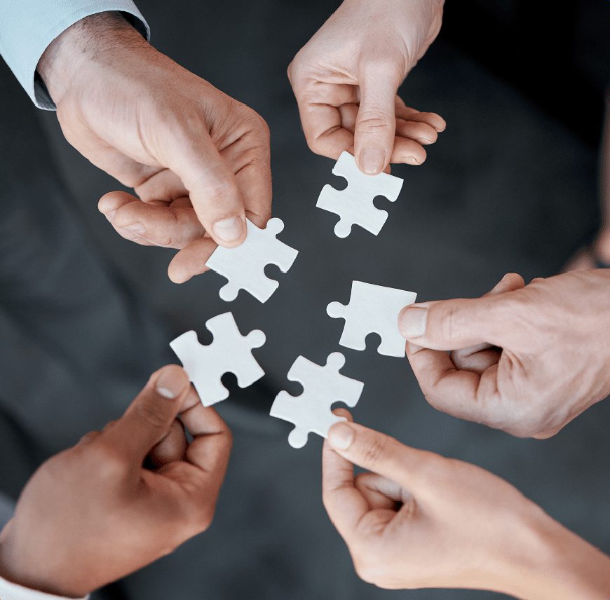 Four hands holding white puzzle pieces about to connect.