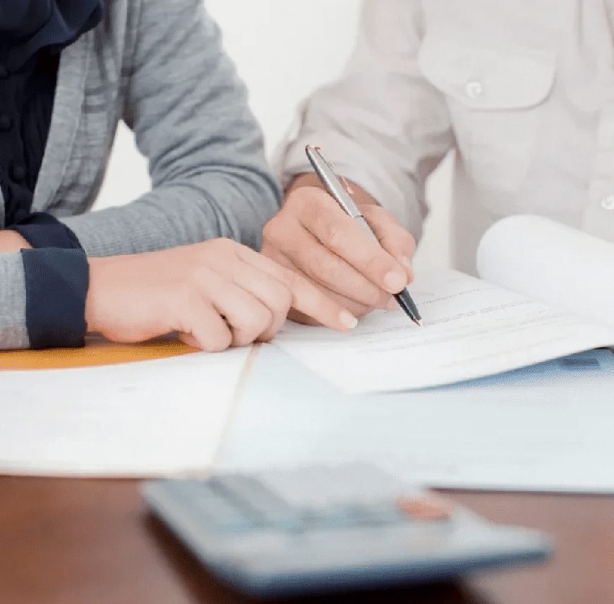 Two people working together on paperwork at a desk.